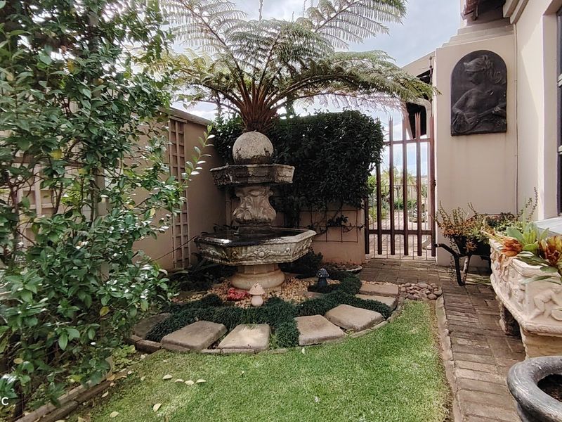 A well-maintained garden area featuring a decorative stone fountain, brick pathways, and secure metal gate access.
