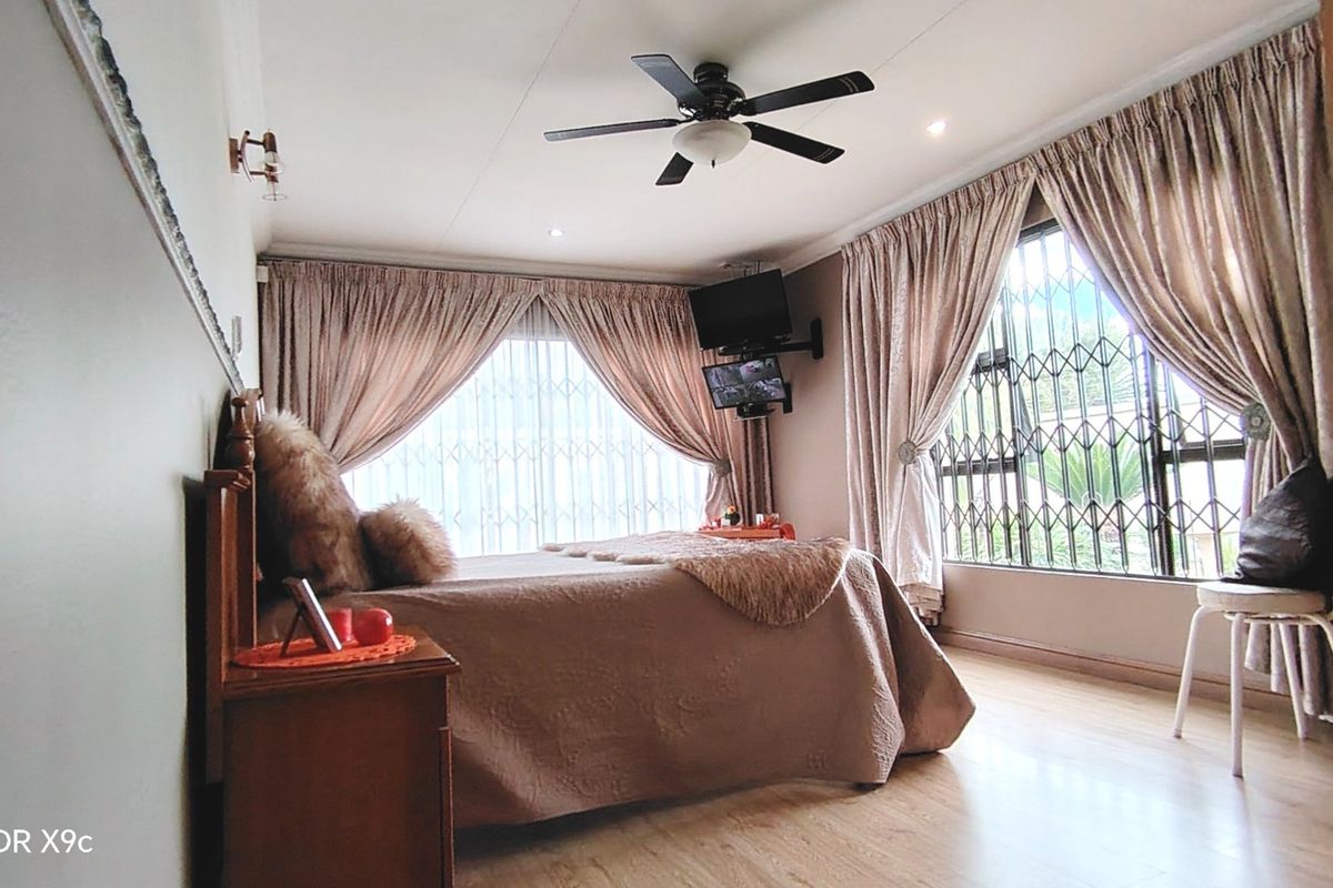 A bedroom featuring laminate flooring, a ceiling fan, and security gates on the windows, providing a functional and secure living space.