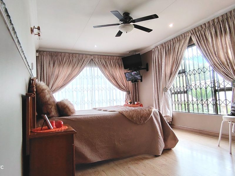 A bedroom featuring laminate flooring, a ceiling fan, and security gates on the windows, providing a functional and secure living space.