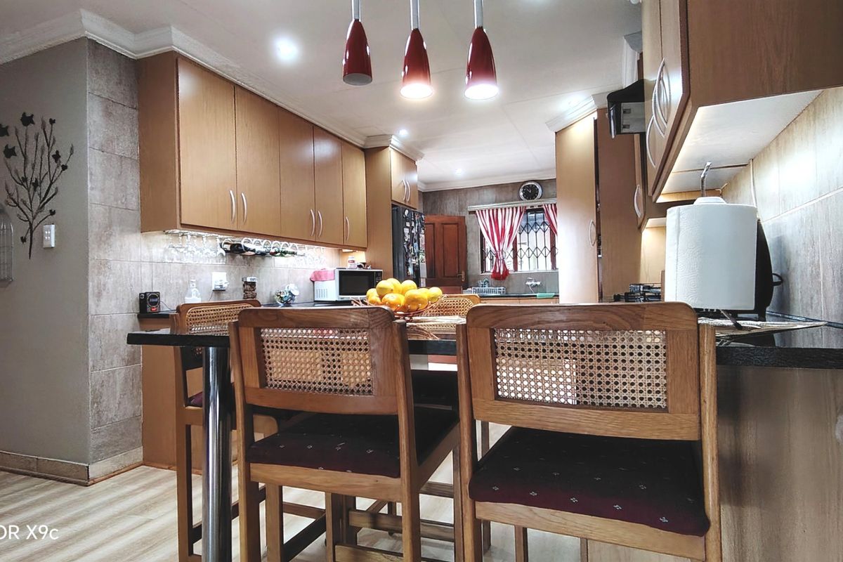 A well-maintained kitchen featuring wood-finish cabinetry, stone countertops, tiled backsplash, and modern recessed and pendant lighting.
