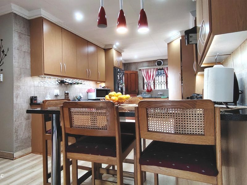 A well-maintained kitchen featuring wood-finish cabinetry, stone countertops, tiled backsplash, and modern recessed and pendant lighting.
