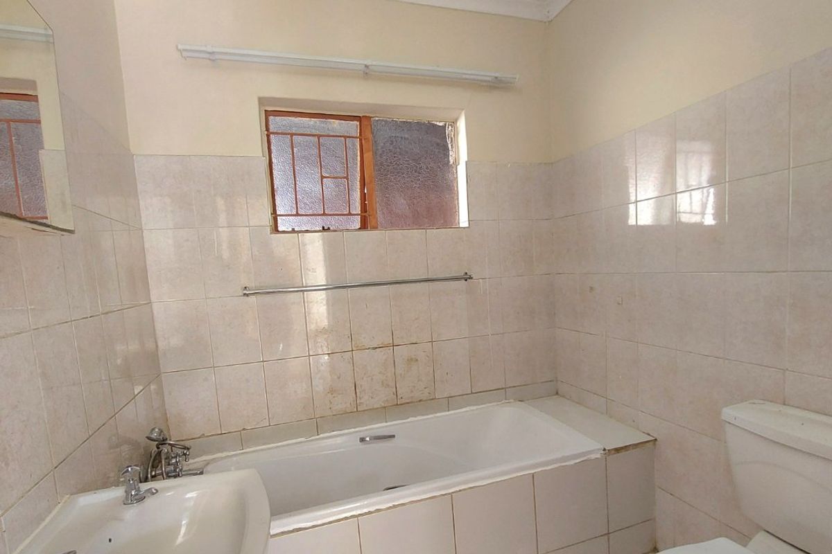 A functional bathroom featuring a pedestal basin, built-in bathtub, and toilet, finished with neutral ceramic tiling throughout.