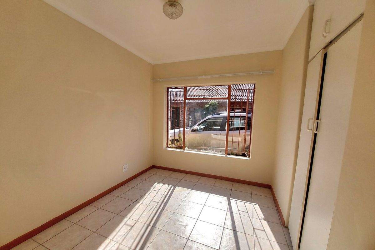 An empty bedroom featuring tiled flooring and built-in cupboards, with a window fitted with security bars.