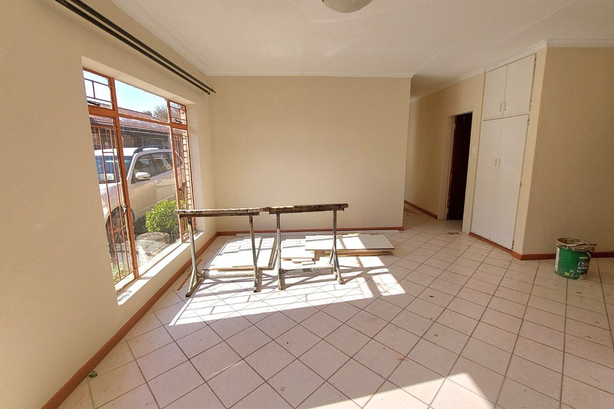 A bright, empty living area featuring tiled flooring, built-in storage cupboards, and a large window allowing for ample natural light.