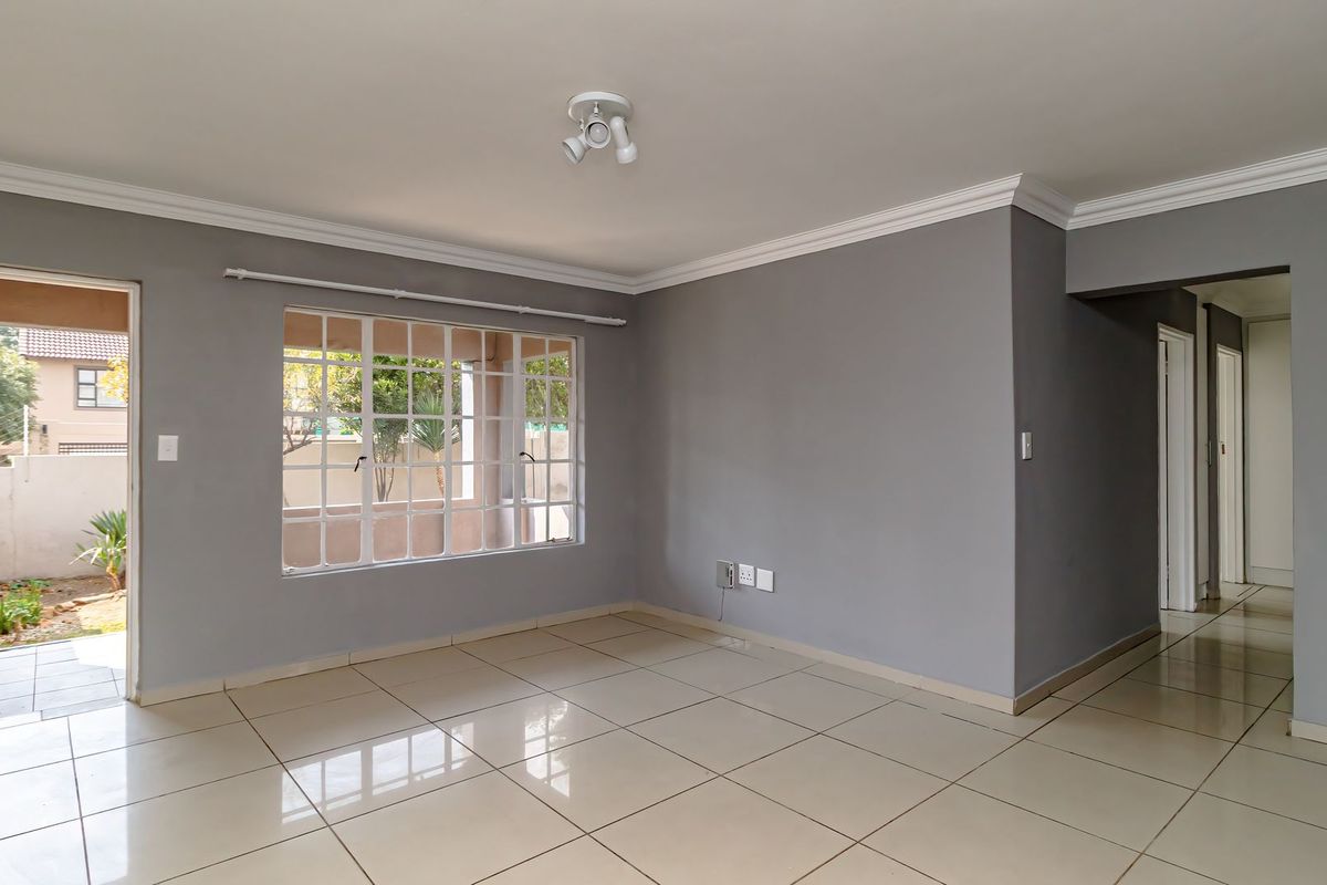 An empty, well-lit living room featuring neutral grey walls, tiled flooring, crown molding, and a large grid-pattern window with direct access to the exterior.