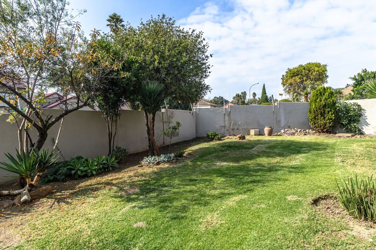 A private rear garden featuring a lawn area enclosed by a perimeter boundary wall with established trees and shrubs.