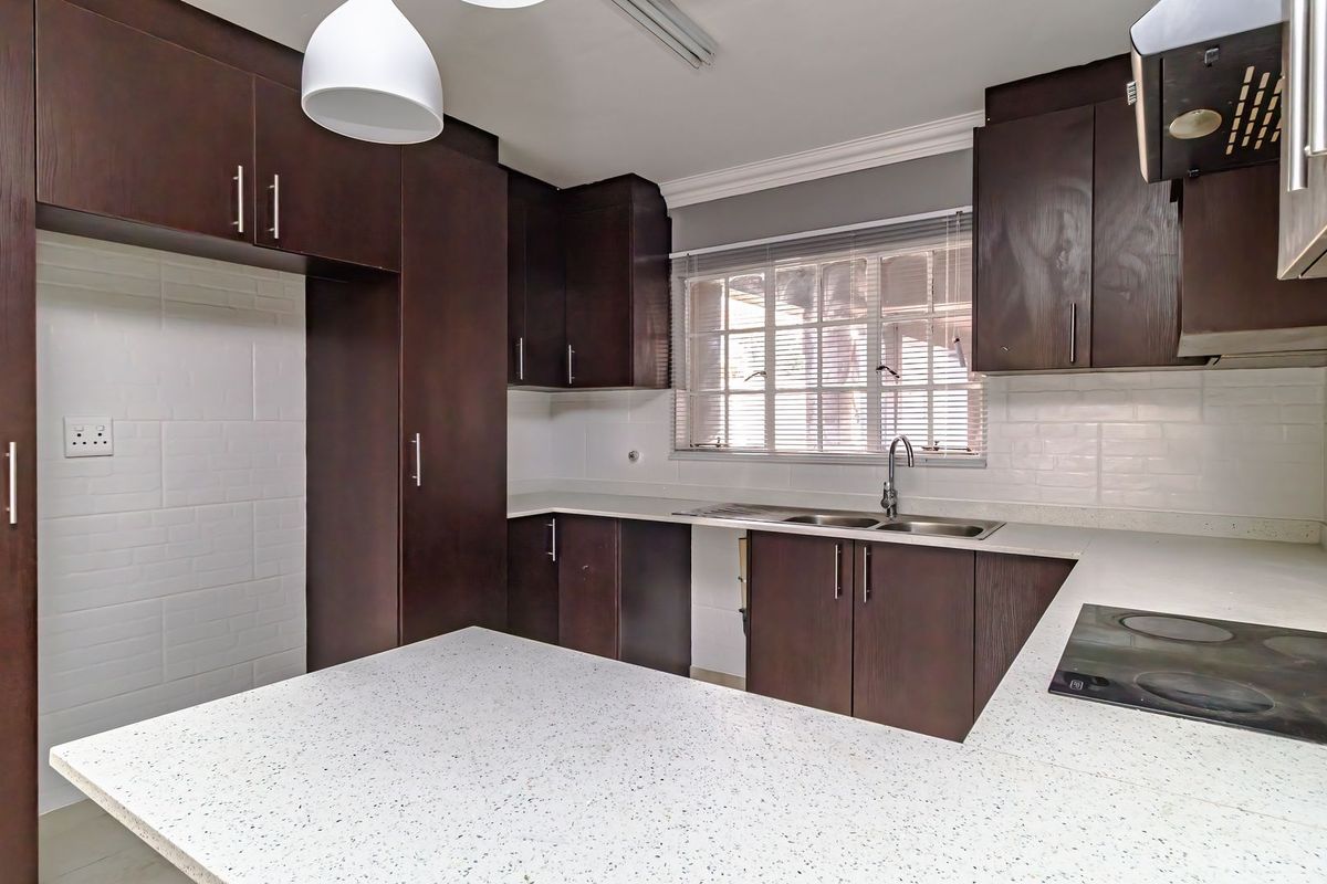 A functional kitchen featuring dark wood cabinetry, white speckled stone countertops, a double basin sink, and a built-in electric hob with an extractor fan.