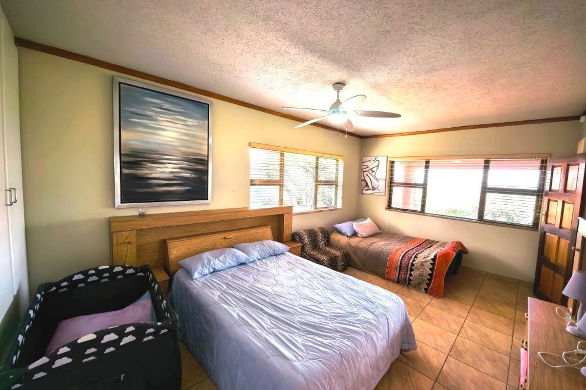 Spacious bedroom featuring tiled flooring, a ceiling fan, and a built-in headboard, offering a functional layout with ample natural light.
