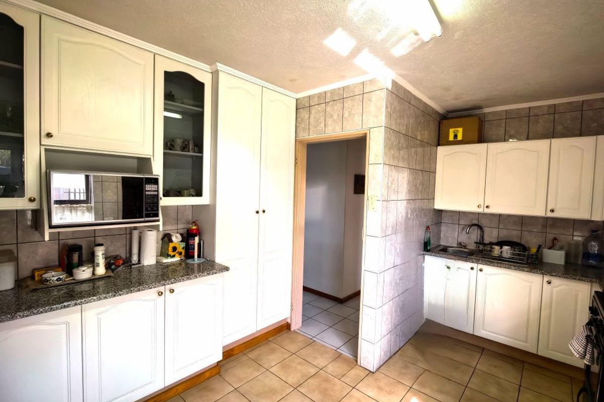 A functional kitchen featuring white cabinetry, granite countertops, built-in microwave, and tiled flooring, offering a practical layout with ample storage space.