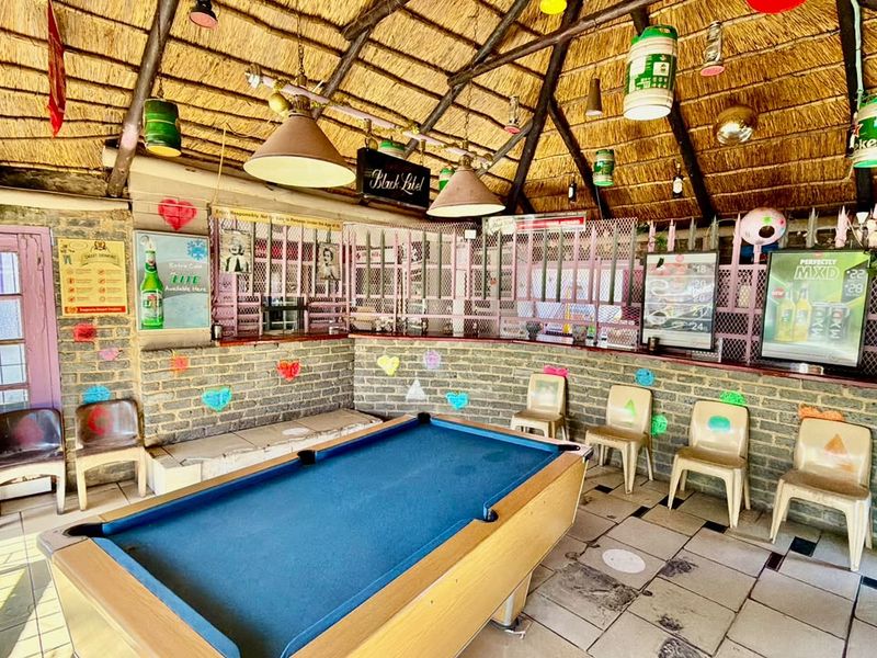 A rustic bar area featuring a thatched roof, exposed timber rafters, brick walls, and a built-in bar counter, suitable for entertainment.