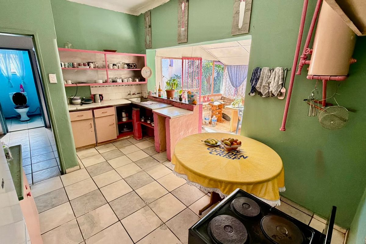 A dated kitchen featuring tiled floors, built-in cabinetry, and an electric stove, with direct access to an adjacent bathroom and outdoor patio area.