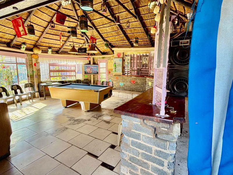 Covered outdoor entertainment area featuring a thatched roof, exposed timber rafters, and a built-in brick bar counter with tiled flooring.
