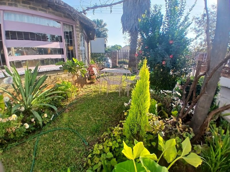 A view of a landscaped garden area featuring a brick facade with a thatched roof and security window bars.