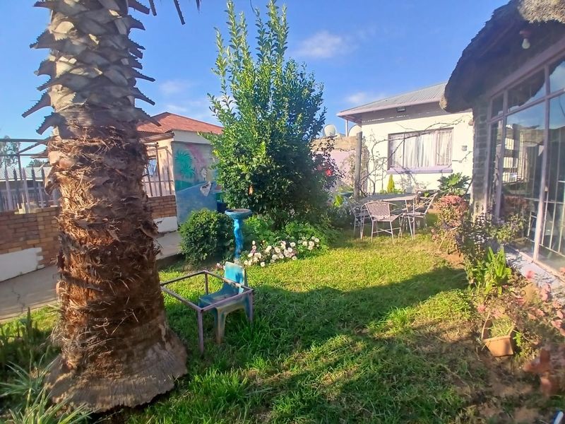 A private garden area featuring a mature palm tree, lawn, and access to the main dwelling via sliding glass doors under a thatched roof.
