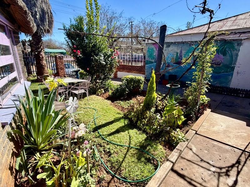 A private garden area featuring a small lawn, paved walkway, and established landscaping, enclosed by brick walls and metal fencing.