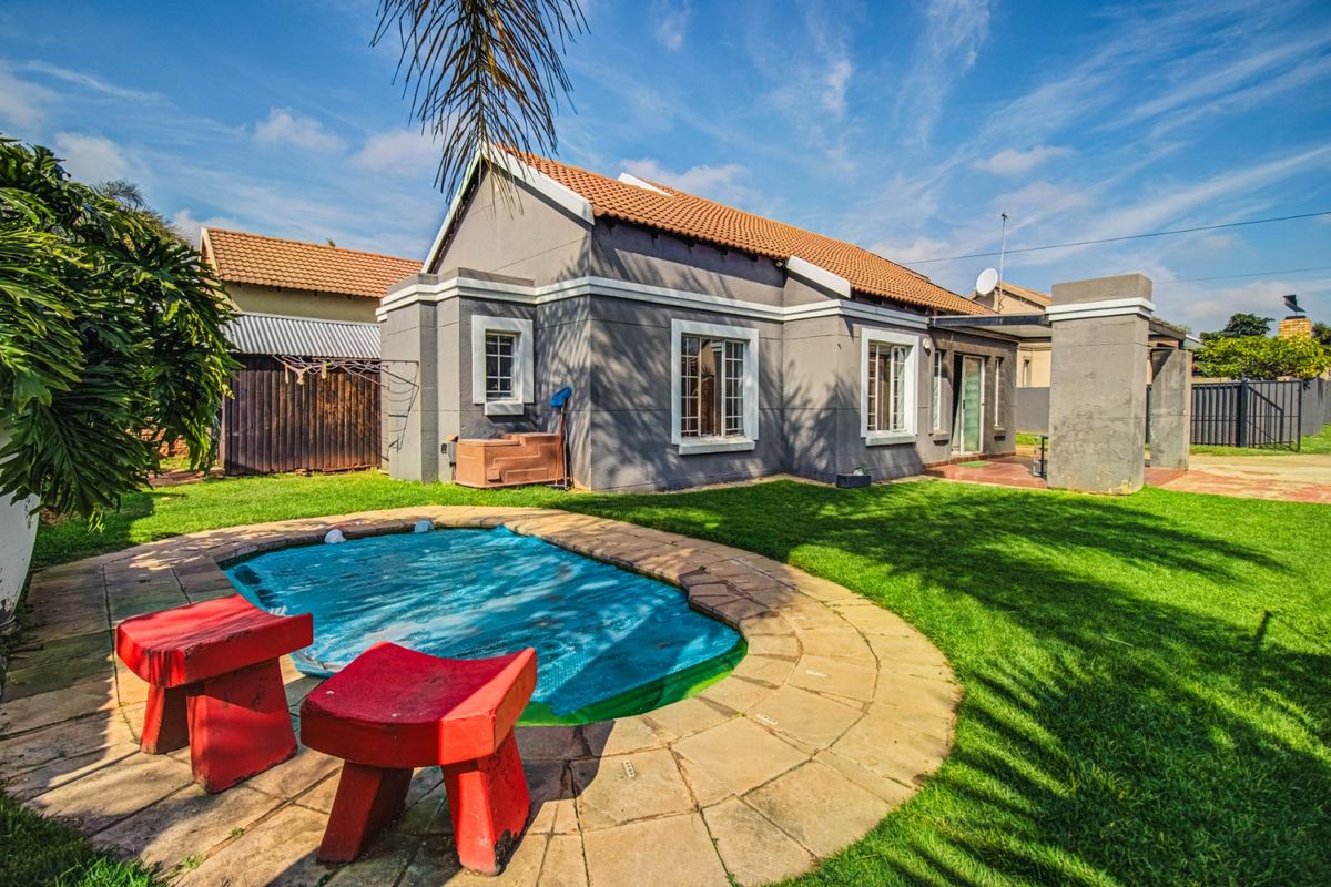 Rear view of the house featuring a swimming pool with a cover, a well-maintained lawn, and a paved patio area.