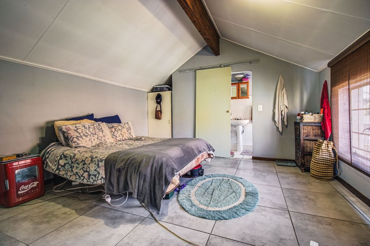 A bedroom featuring a vaulted ceiling with exposed timber beam, tiled flooring, and an en-suite bathroom accessed via a sliding door.