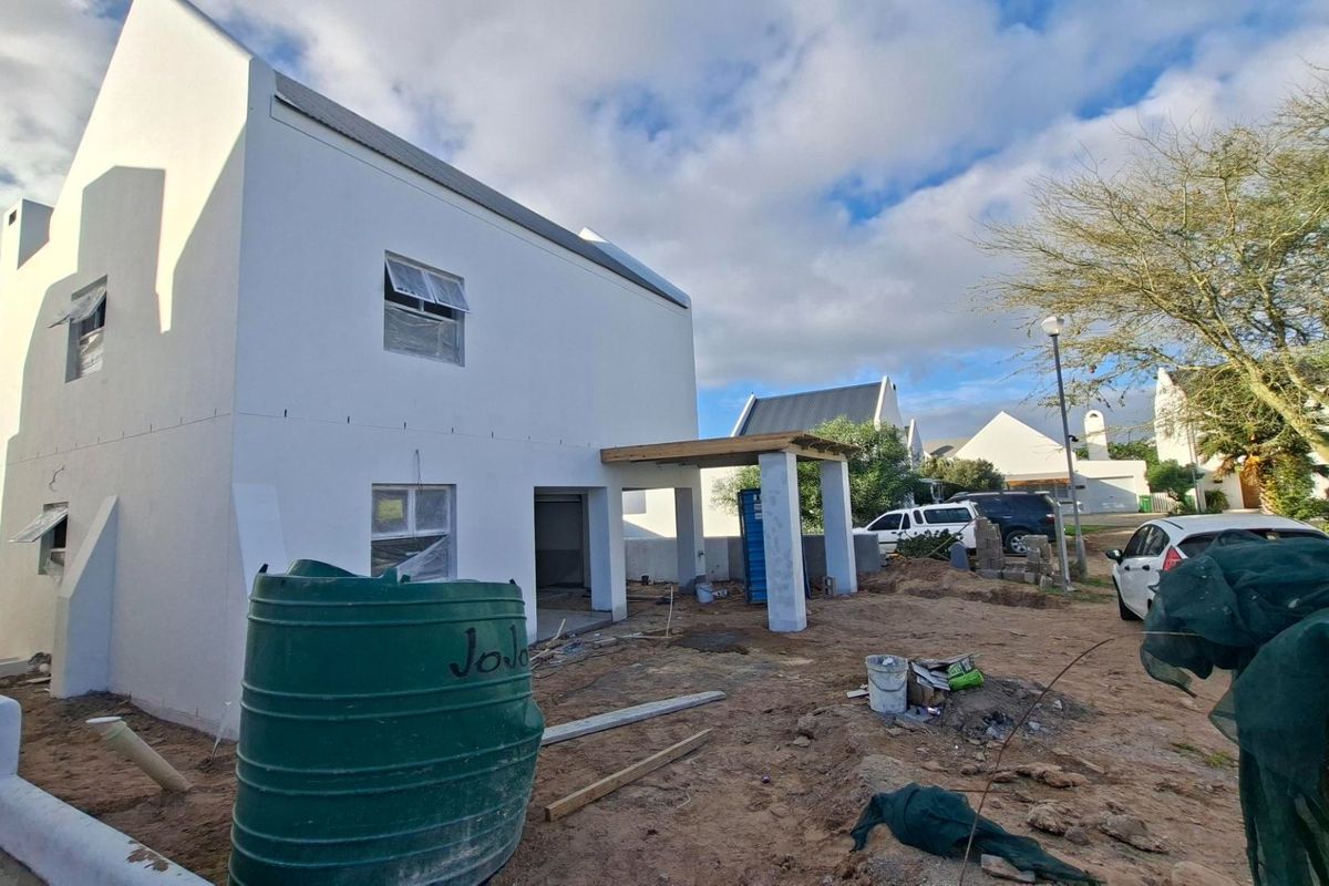 Rear view of a residential property under construction, featuring a white facade, covered patio area, and an installed water storage tank.