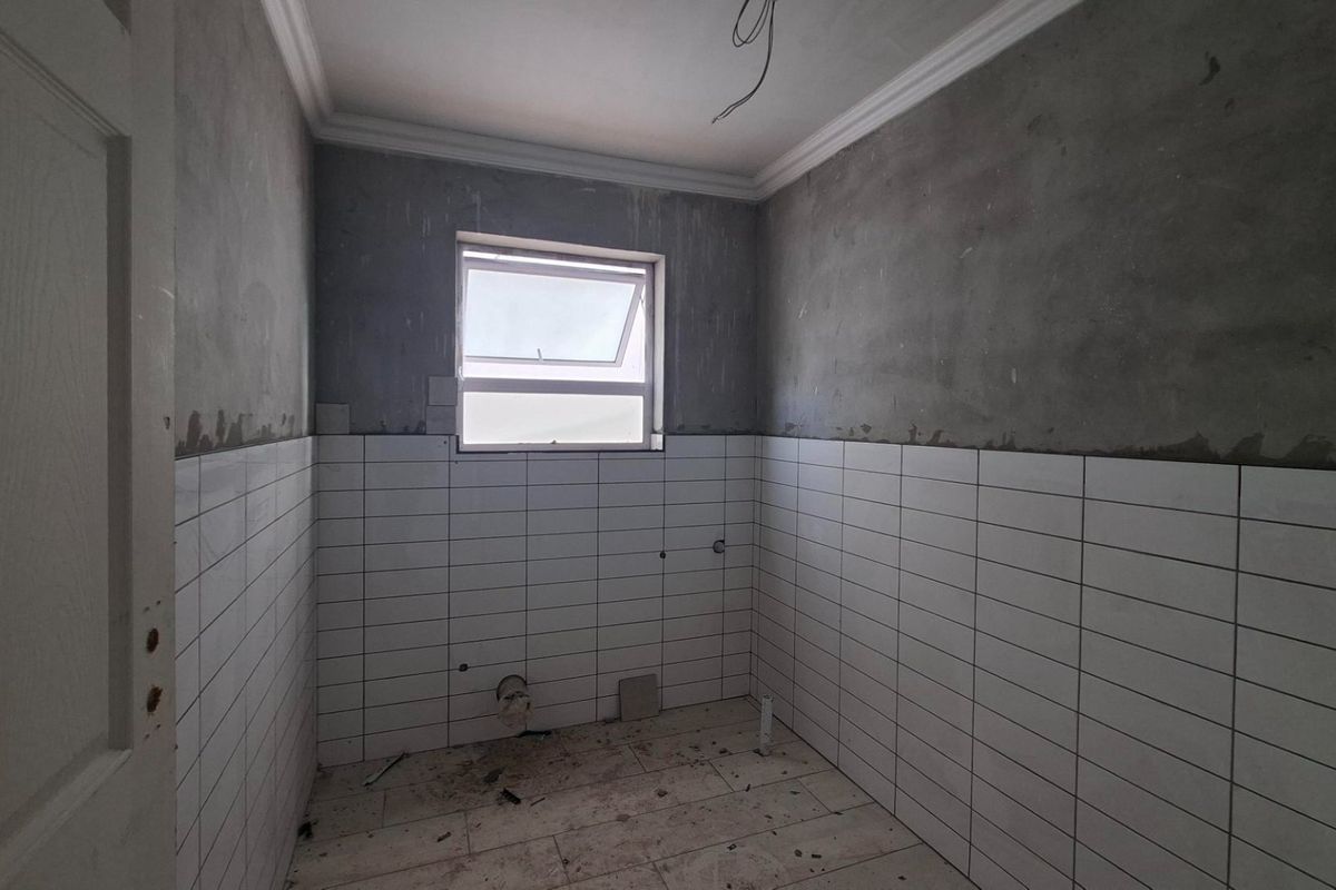 An unfinished bathroom space featuring partially tiled walls, tiled flooring, and a top-hung window, currently undergoing renovation.