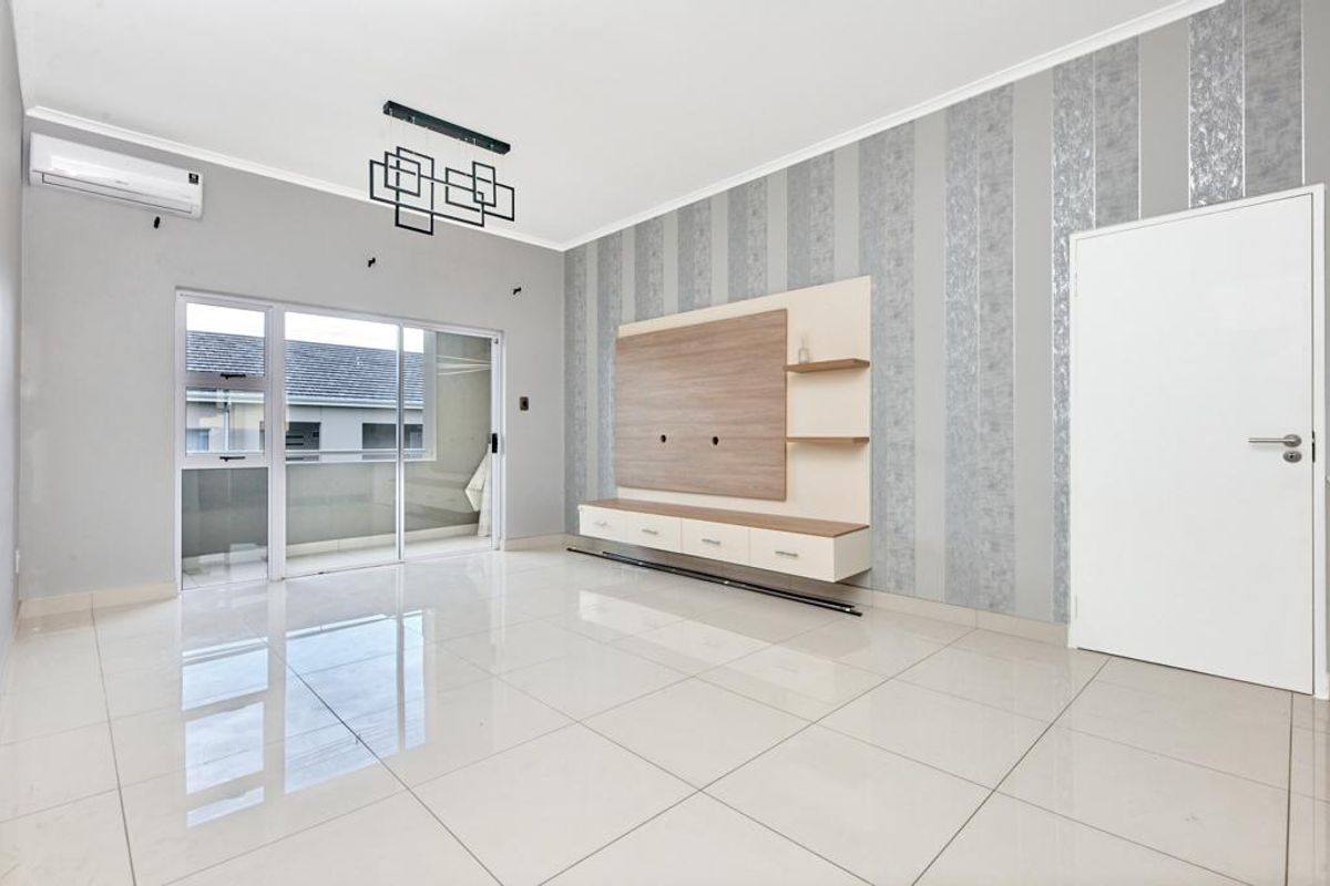 A bright, empty living room featuring polished floor tiles, a built-in media console, a feature wall, and direct access to a private balcony.