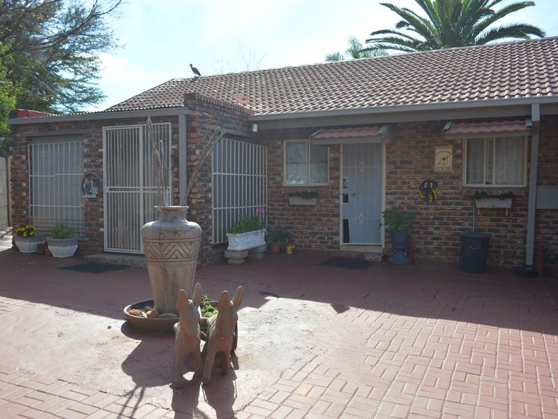 A rear exterior view of a face-brick house featuring a paved courtyard area and secure metal gates.