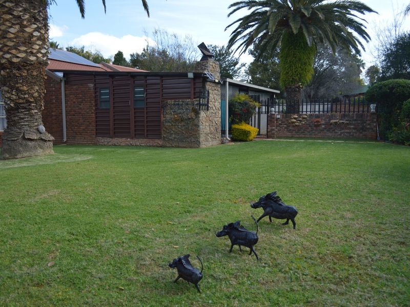 A spacious rear garden featuring a well-maintained lawn, mature palm trees, and a brick-built exterior with a stone chimney and solar panels.