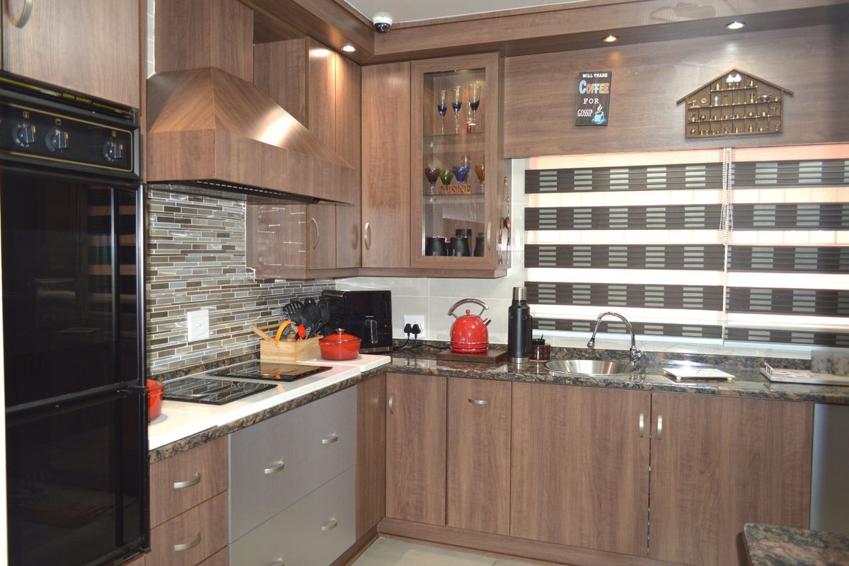 A well-maintained kitchen featuring wood-finish cabinetry, granite countertops, a mosaic tile backsplash, and integrated appliances including an oven and hob.
