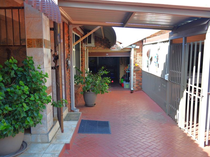 A paved exterior entrance area featuring a covered carport, brick facade, and access to a garage with security gate.