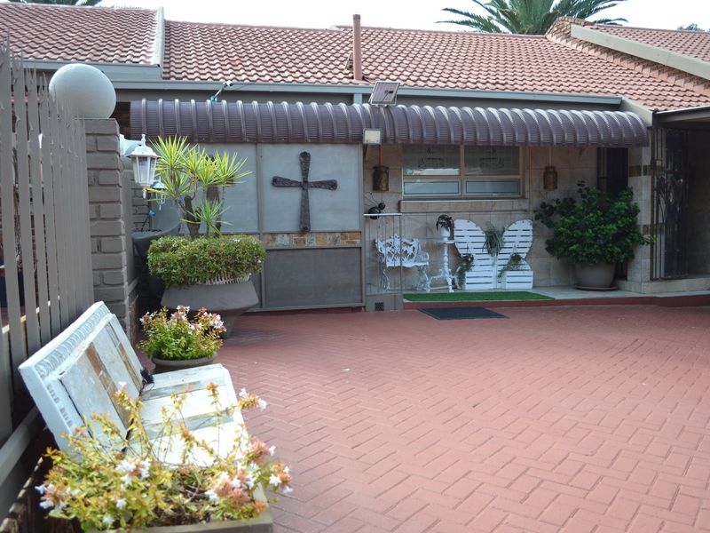 Front entrance area featuring brick paving, a covered patio section with a metal awning, and secure boundary walling.
