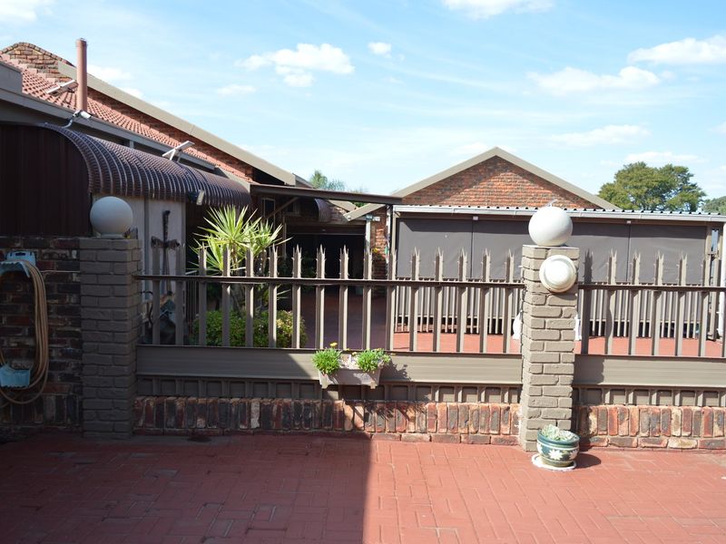 A rear exterior view featuring brick paving, a covered patio area, and secure metal fencing with brick pillars.