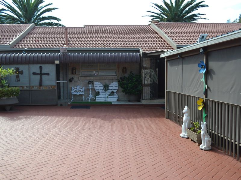 A paved rear courtyard area featuring a covered patio with outdoor blinds and terracotta roof tiles.