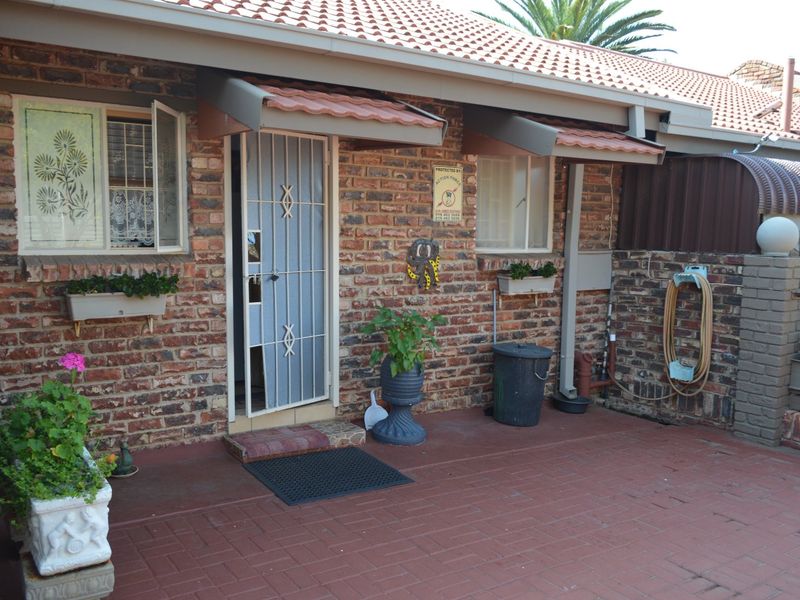 A rear exterior view of the house featuring a face brick facade, paved patio area, and a secure entrance with a metal security gate.