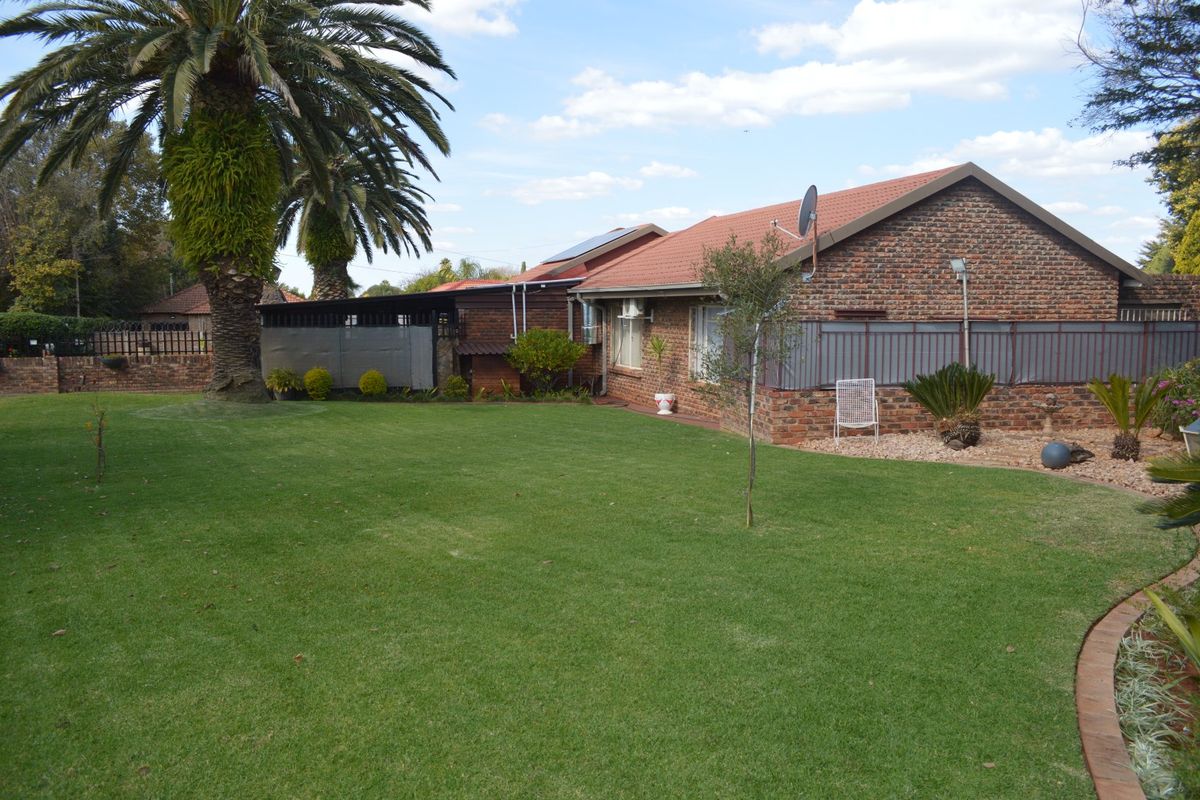 A well-maintained rear exterior view of a face brick house featuring a spacious lawn, mature palm tree, and solar water heating installation.