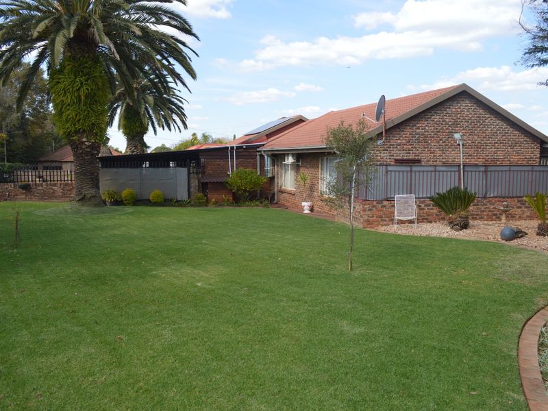 A well-maintained rear exterior view of a face brick house featuring a spacious lawn, mature palm tree, and solar water heating installation.