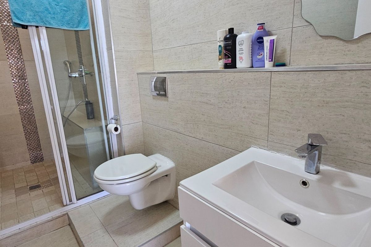 Modern bathroom featuring a wall-mounted toilet, glass shower enclosure, and a vanity basin with neutral tiled finishes throughout.