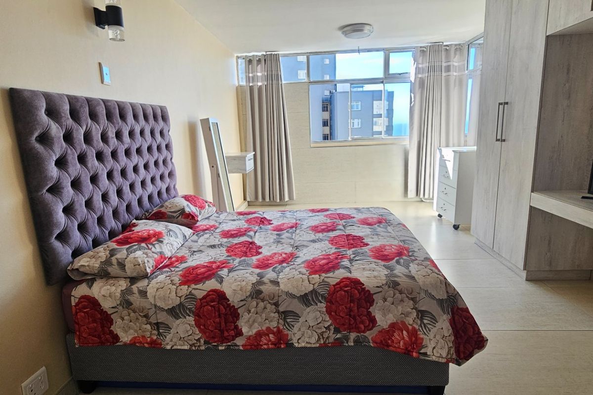 A well-lit bedroom featuring built-in cupboards, tiled flooring, and a large window providing natural light and urban views.