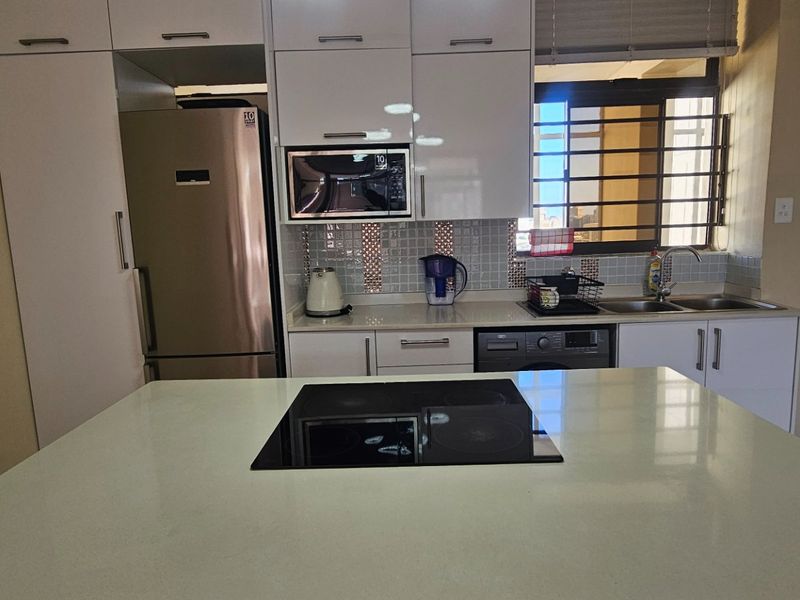 Modern kitchen featuring white cabinetry, stone countertops, a central island with an integrated electric hob, and a tiled backsplash.