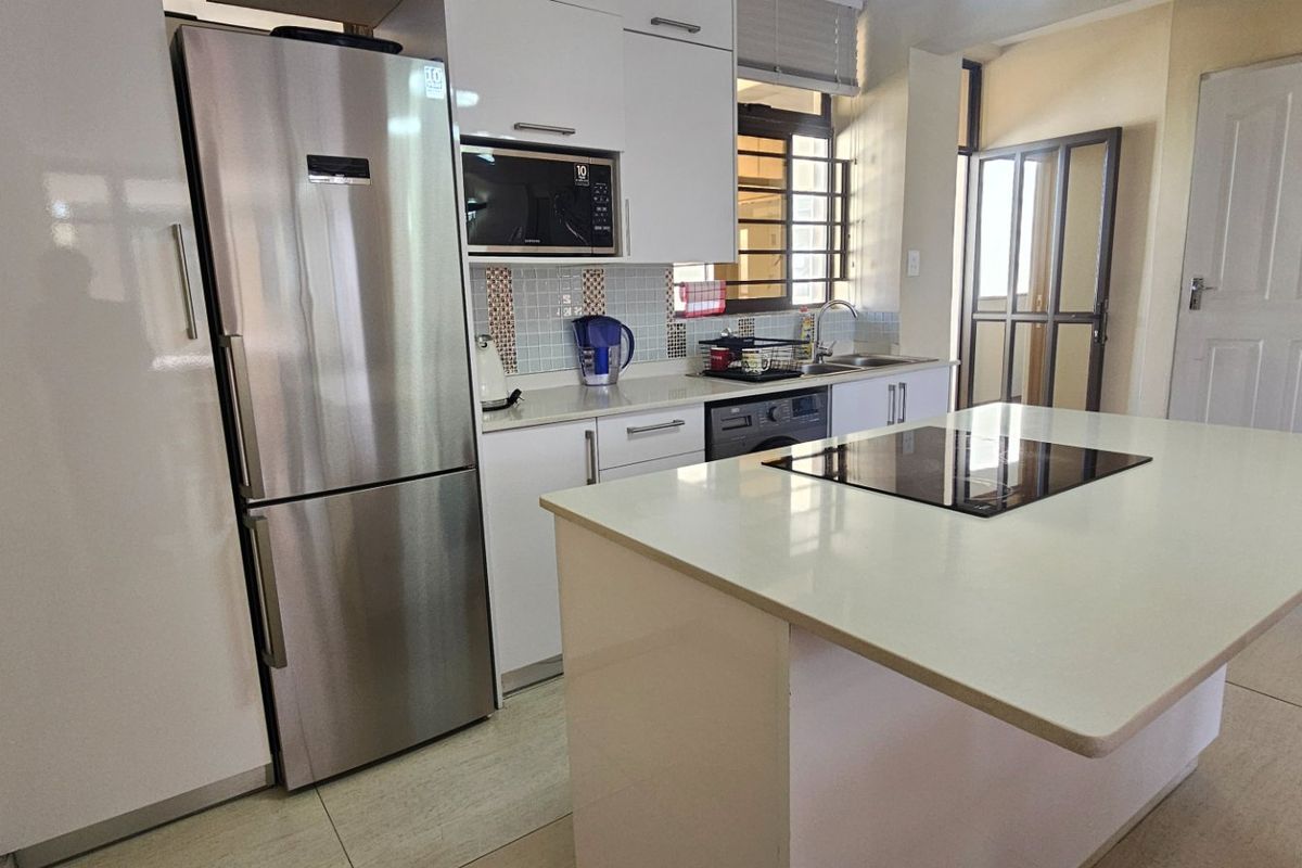 Modern kitchen featuring white cabinetry, a central island with an integrated hob, tiled backsplash, and stainless steel appliances.
