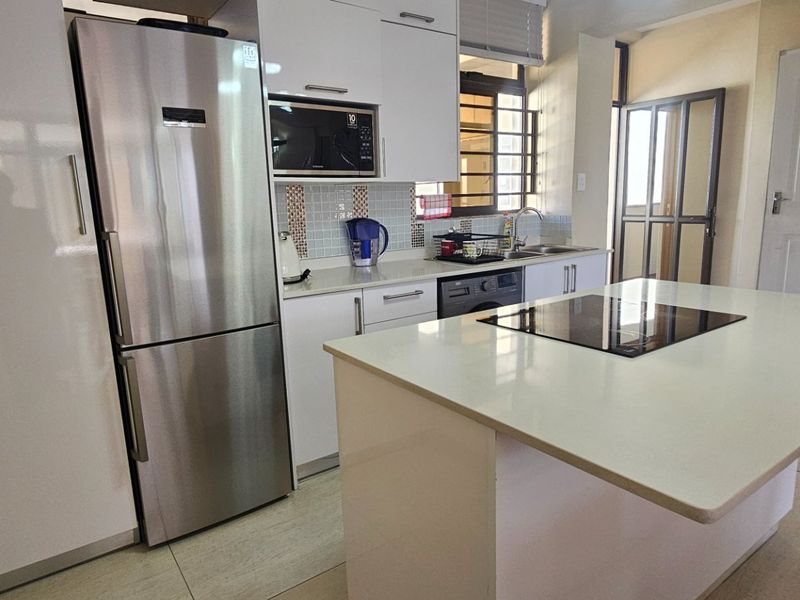 Modern kitchen featuring white cabinetry, a central island with an integrated hob, tiled backsplash, and stainless steel appliances.