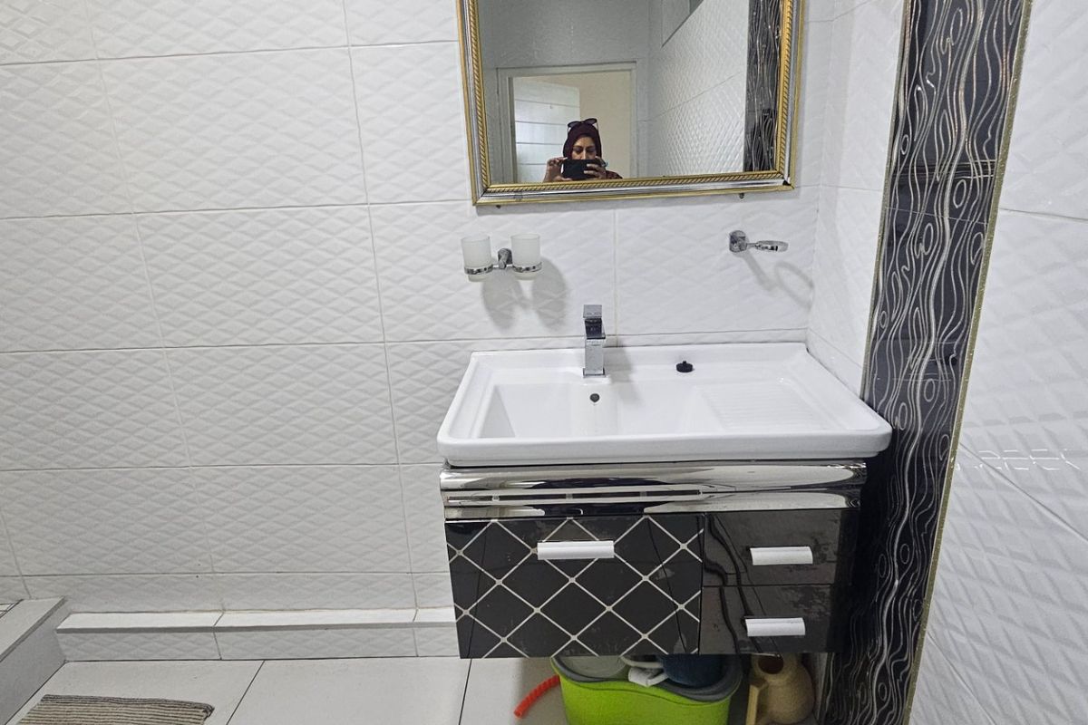 A functional bathroom featuring a modern vanity cabinet with a basin, wall-mounted mirror, and tiled finishes throughout.