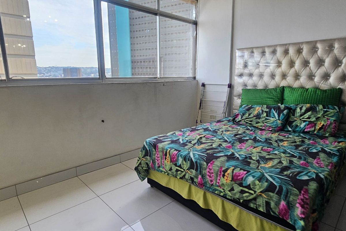 A bedroom featuring large windows with city views and tiled flooring.