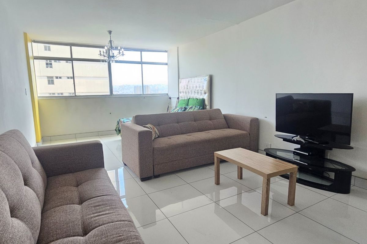 A spacious living area featuring large windows that provide natural light and tiled flooring throughout.
