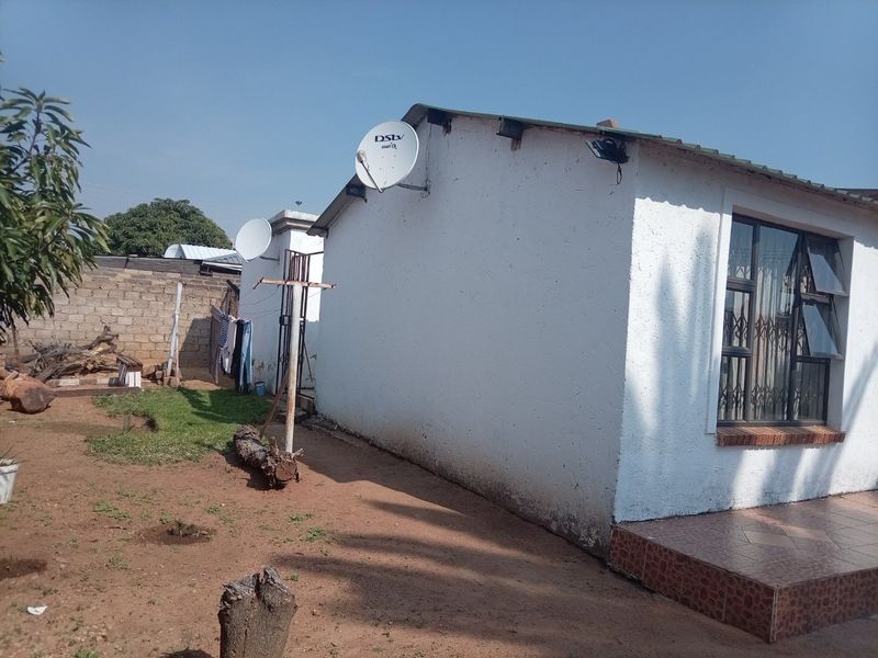 Rear exterior view of the house featuring a tiled patio step, security-barred windows, and a satellite dish installation against a concrete block boundary wall.