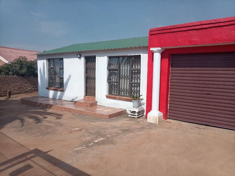 Front view of a single-story house featuring a tiled entrance porch, metal security gates, and an attached garage with a roller shutter door.