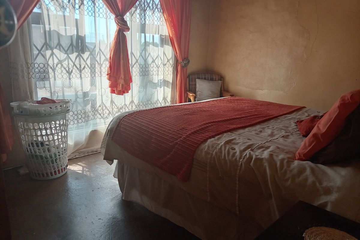 A bedroom featuring concrete flooring and a security gate over the window, showing signs of wear on the wall surfaces.
