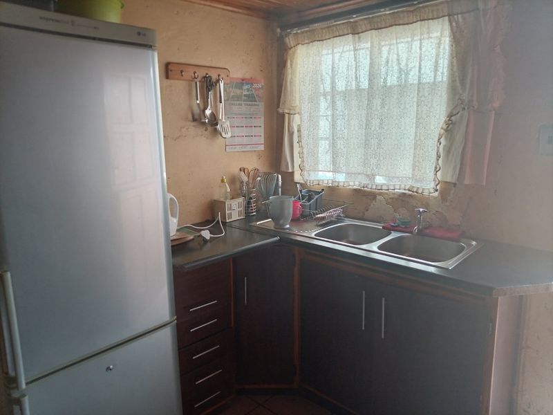 A compact kitchen featuring dark cabinetry, a double bowl sink, and laminate countertops, requiring wall repairs and cosmetic updates to improve the space.