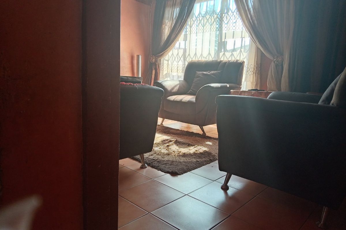 A living room area featuring tiled flooring and a window with security gate, providing natural light to the space.