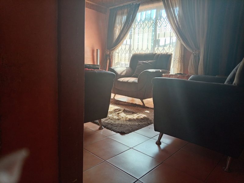 A living room area featuring tiled flooring and a window with security gate, providing natural light to the space.