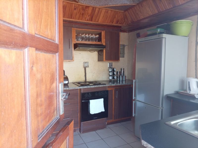 Compact kitchen featuring dark wood cabinetry, granite countertops, built-in oven and hob, and distinctive timber ceiling paneling.