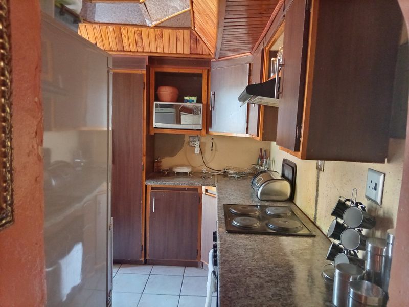 A dated kitchen featuring timber ceilings, laminate countertops, and an electric hob, requiring cosmetic updates and wall repairs to improve functionality and aesthetic appeal.